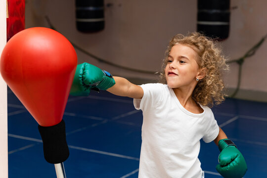 Little girl strongly and emotionally hits the punching bag. Selective focus, photo in motion for projects or design about the development of sports of younger generation