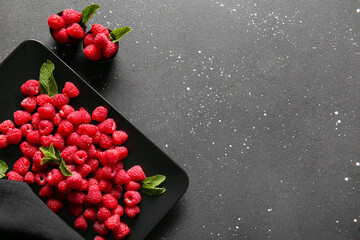 Plate and bowls with fresh raspberries on black background