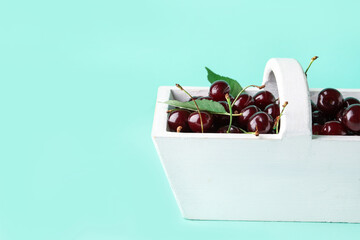Basket with sweet cherries and leaves on blue background