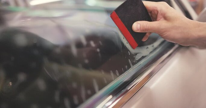 Car tinting windows - Worker specialist apply tint foil on car window in workshop video 4K