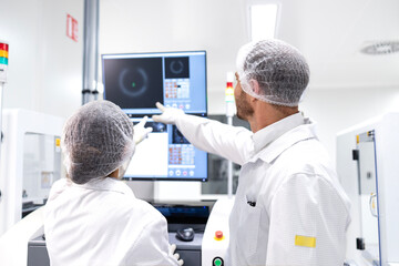 Factory coworkers analyzing production and checking monitors at assembly line.