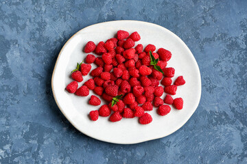 Plate with fresh raspberries and mint on blue background