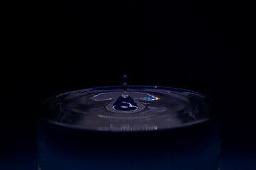 Drop of water falling into a glass with blue light on black background