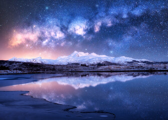 Bright Milky Way over snowy mountains and sea coast at winter night. Landscape with snowy rocks,...