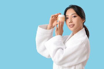 Beautiful young Asian woman with facial cream on blue background - obrazy, fototapety, plakaty