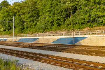 Electrified railway line, near railway station. In the background is a retaining wall and green...