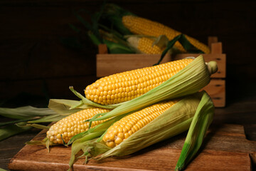 Board and box with fresh corn cobs on wooden table