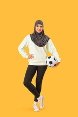 Fototapeta premium Young Muslim woman with soccer ball on yellow background