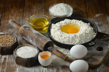 Kneading dough with flour and eggs, with kitchen accessories, on table and old background.