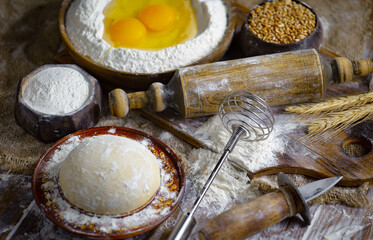 Kneading dough with flour and eggs, with kitchen accessories, on table and old background.