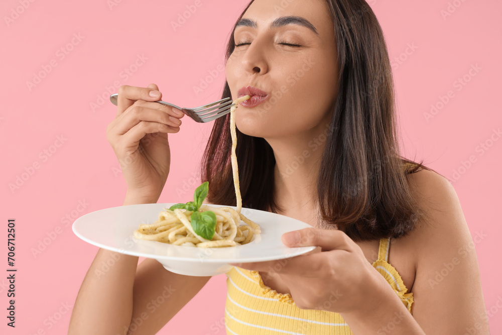 Canvas Prints Young woman eating tasty pasta on pink background, closeup