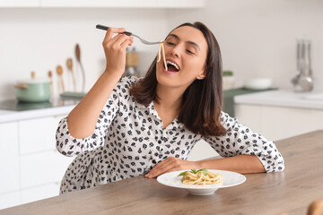 Young woman eating tasty pasta at table in kitchen