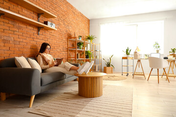 Young woman writing in notebook on sofa at home office
