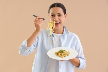 Young woman eating tasty pasta on beige background