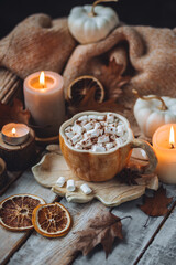 Fototapeta na wymiar Spicy sweet fall hot drink: delicious pumpkin latte with cinnamon, marshmallow with salted caramel. Served in handmade artisan mug in shape of pumpkins, cozy home decor with candles, dry autumn leaves