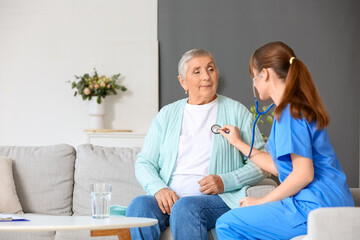 Fototapeta premium Young caregiver hearing senior woman with stethoscope at home