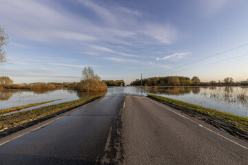 Natural disaster, spring flood. The road in the countryside is flooded with water, the river is...