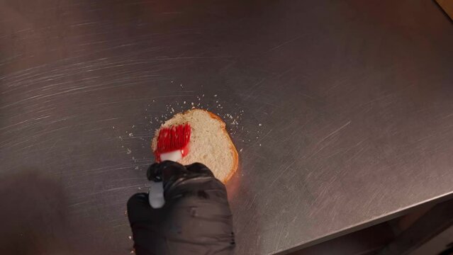 Chef in black gloves making burge. spread sauce on bun. Close-up of a skilled craftsman working at the workplace 