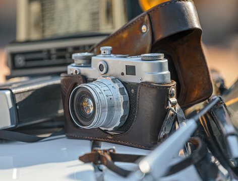 An old, vintage film camera with a lens and a brown leather case on a blurred background. Small vintage analog photo camera with black leather strip. Old camera on a tripod.