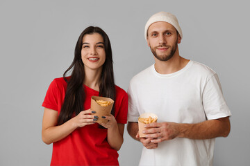 Beautiful young couple with french fries on grey background