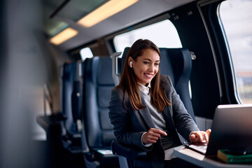 Smiling female entrepreneur surfing the net on laptop while traveling by train. - obrazy, fototapety, plakaty