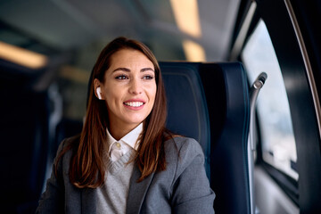 Smiling woman listens music over earphones while traveling by train.
