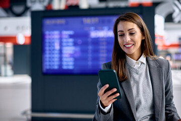 Happy businesswoman using app on cell phone while waiting for train ride.