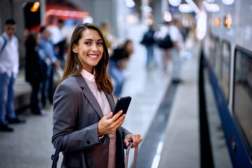 Young happy woman using cell phone while waiting for train at station.