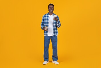 Fototapeta premium Smiling young black man holding takeaway coffee and smartphone