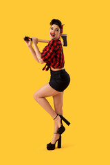 Fototapeta na wymiar Young pin-up woman with axe on yellow background