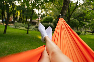Horizontal shot of a woman's leg resting on an orange hammock hanging from a tree in a park. The concept of holidays, vacations, recovery after a hike