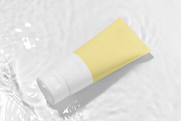 Yellow and white blank mockup tube of moisturizing cream in waves of water on a white background. Concept of natural beauty products and skin care for face and body