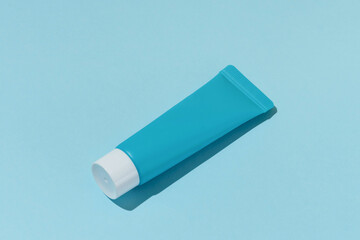 Blue mockup of a tube of face or under eye cream on a blue isolated background with direct lighting. Concept of beauty products to moisturize and nourish the skin