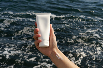 Female hand with smear sample holding a white mockup jar of moisturizer or sunscreen for face and...