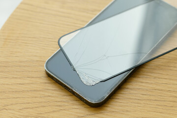 Close-up of the broken protective glass of the phone removed from the screen on a wooden...