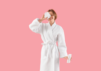 Beautiful young woman in bathrobe, with bast wisp and shower gel on pink background