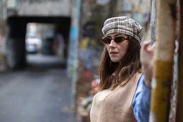 young woman with sunglasses and hat leaning against a graffiti wall