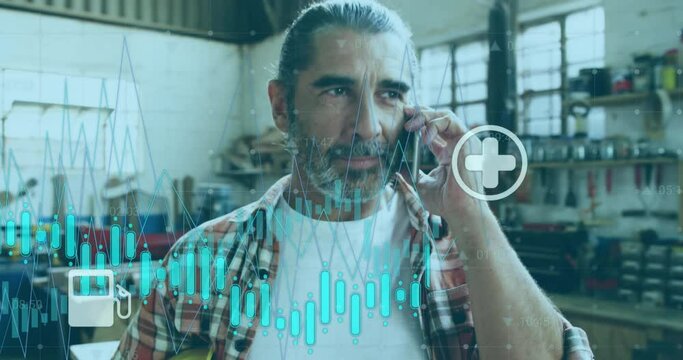 Animation of graph with energy and media icons over mature caucasian male carpenter talking on phone