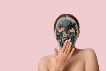 Surprised young woman with activated charcoal mask on her face against pink background