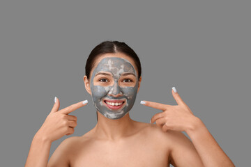 Young woman with clay mask on her face against grey background