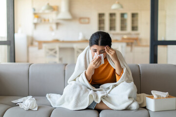 Ill indian woman blowing her nose with tissue at home - obrazy, fototapety, plakaty