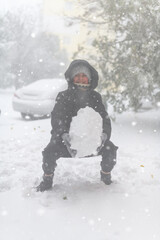 a girl is playing with snow on the street, it is snowing, a blizzard and frost on a winter day
