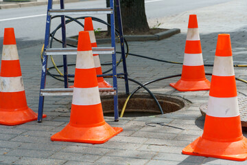Orange cones installed around the dangerous area on the sidewalk. An open travel hatch. Laying of a...