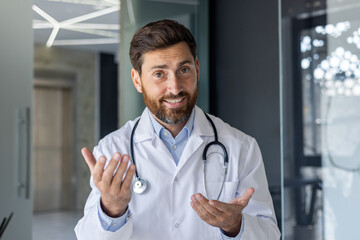 Close-up portrait of a young smiling male doctor who is in the hospital and talking via video link,...