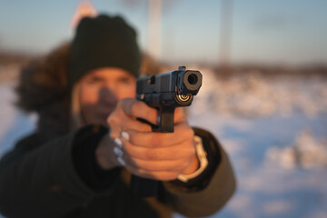 A girl takes aim with a 9mm tactical pistol outdoors in winter. Soft focus photo.