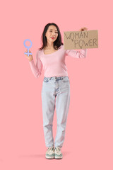 Young Asian girl holding paper with text WOMAN POWER and gender symbol on pink background