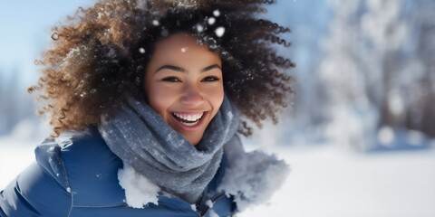Beautiful young African American woman having fun outdoors in the snowy winter, smiling and looking at the camera, wearing a blue jacket. Female person enjoying cold weather outside, joyful lady - obrazy, fototapety, plakaty