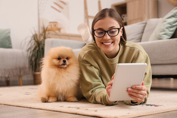 Young woman with cute Pomeranian dog using tablet computer on floor at home - Powered by Adobe