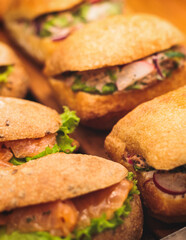 Beautifully decorated catering banquet table with different food snacks and appetizers setting with sandwiches, bagels, baguette club submarine sandwich, on wooden plate, on party or celebration