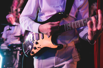 Concert view of an electric guitar player with vocalist and rock band performing in a club, male musician guitarist on stage with audience in a crowded concert hall arena - obrazy, fototapety, plakaty